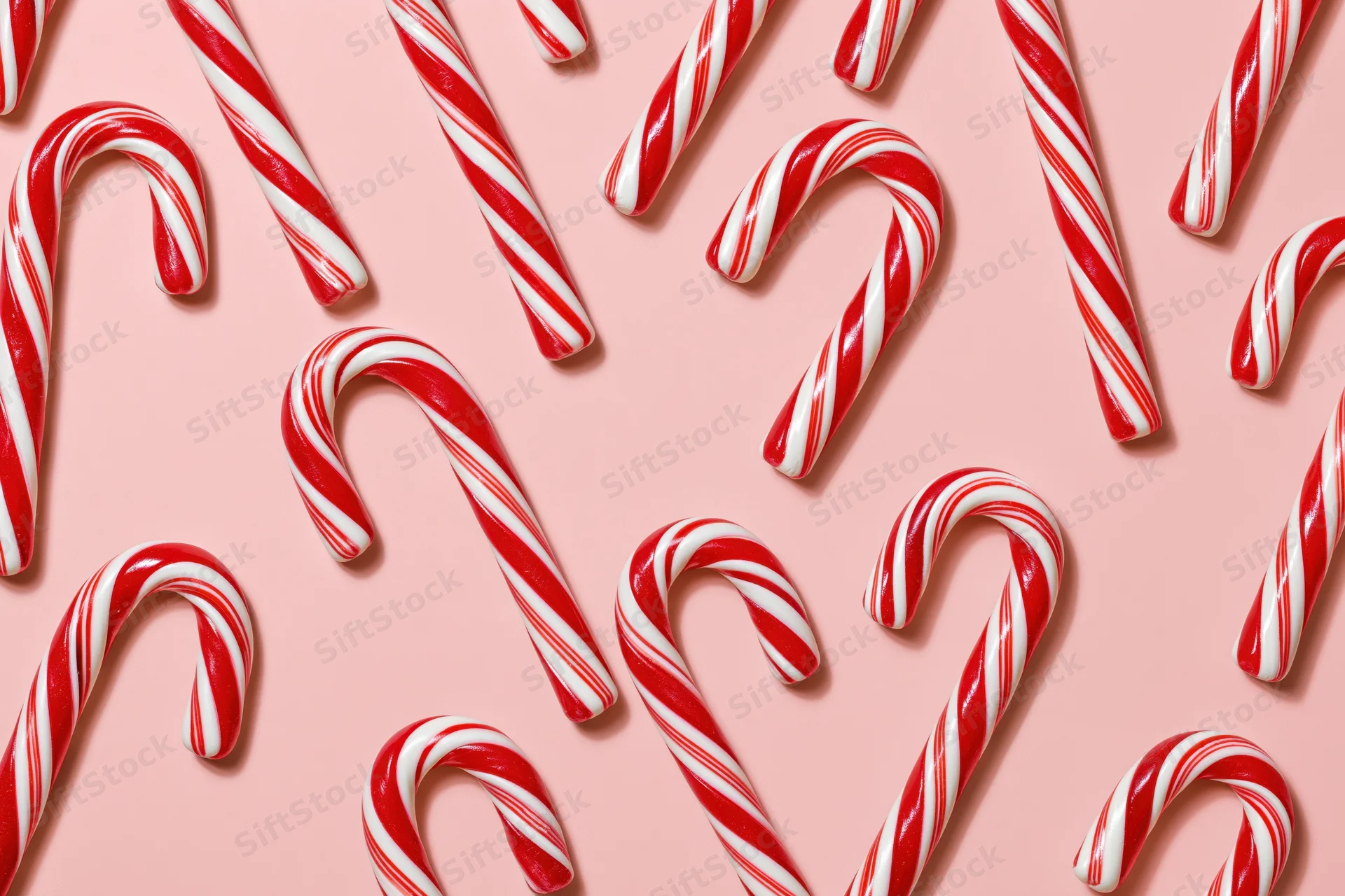 Candy canes arranged in scattered pattern on pink surface