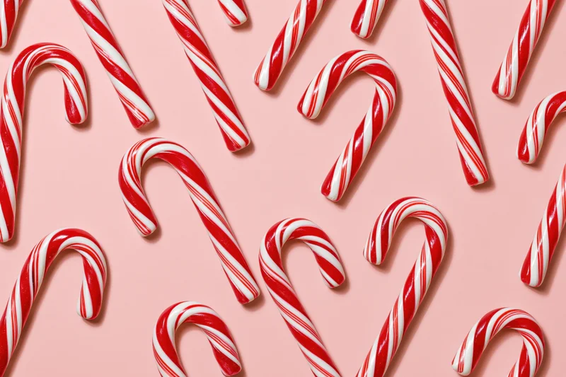 Candy canes arranged in scattered pattern on pink surface