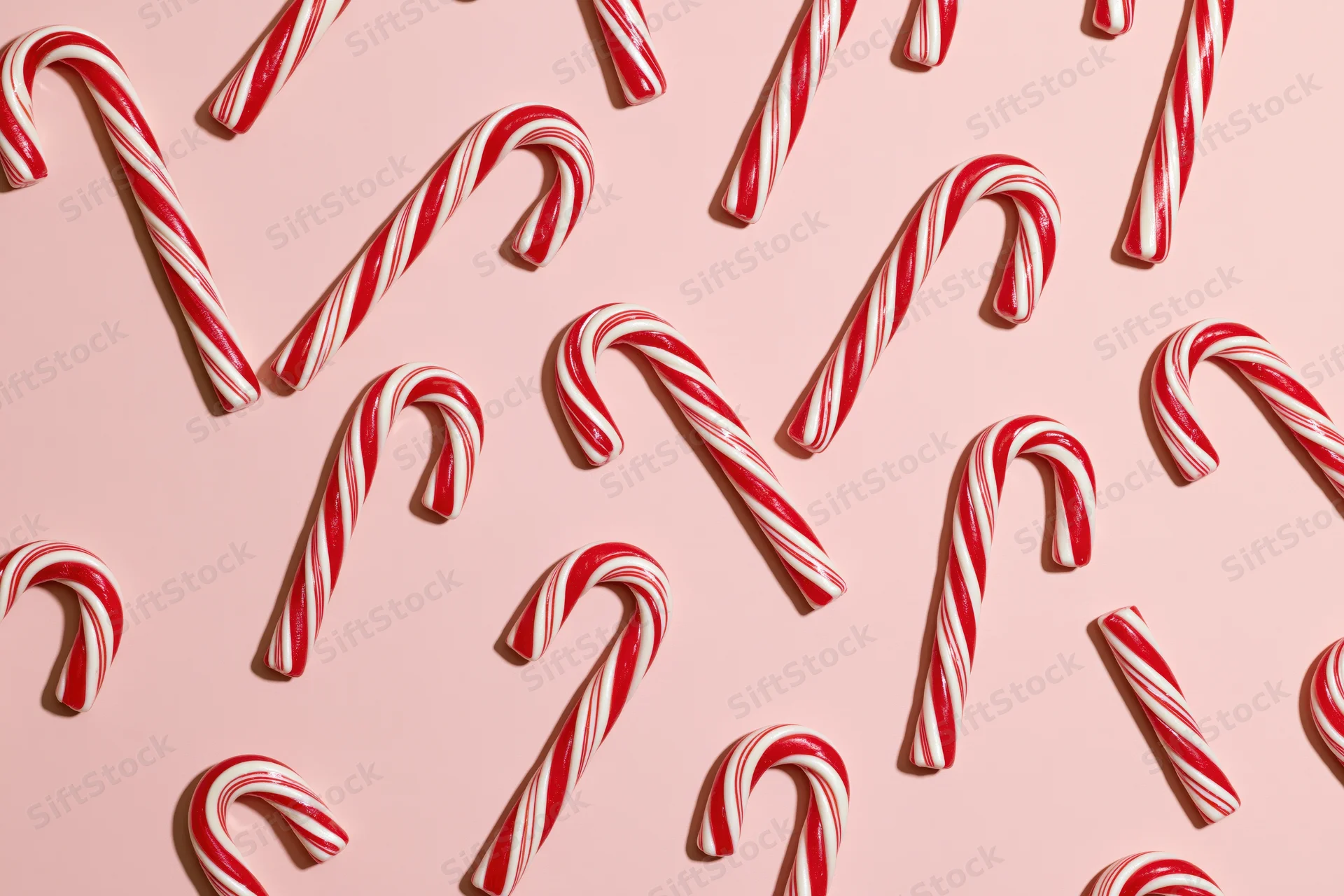 Candy canes scattered in a flat lay on a pink surface