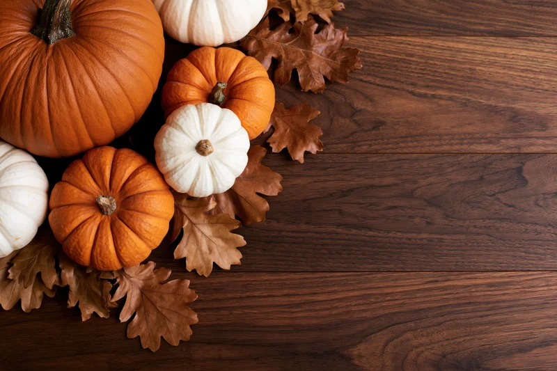 Pumpkins and dried oak leaves arranged in corner on dark wooden table