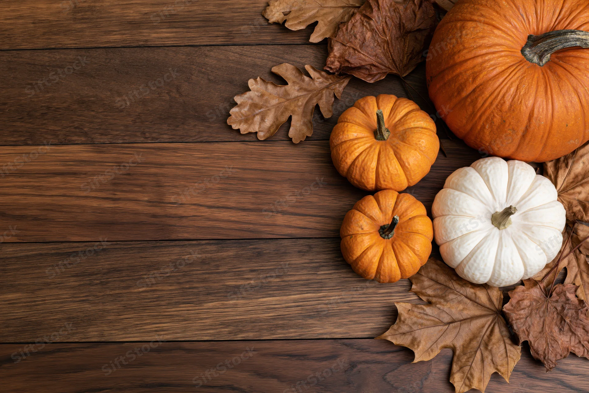 Pumpkins and dried leaves arranged on a wooden table with copyspace