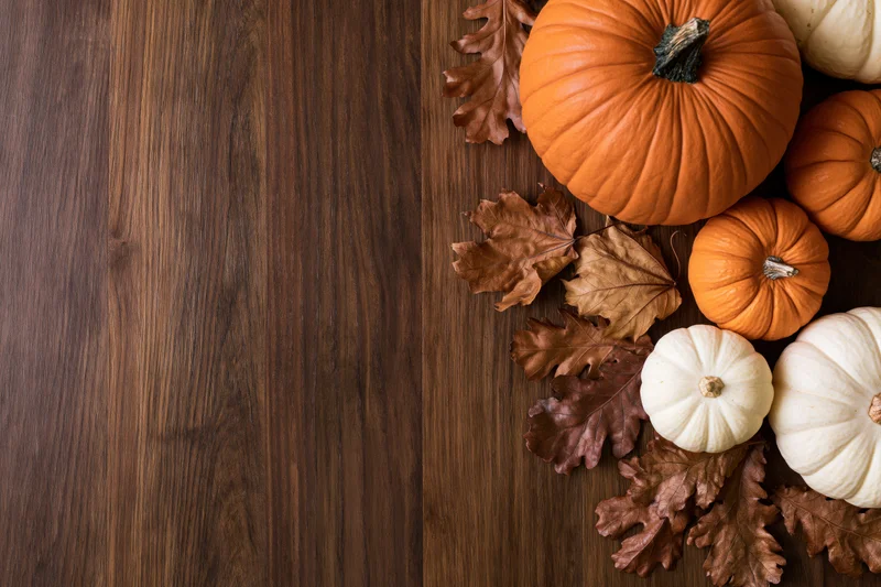 Pumpkins and dried leaves arranged on a wooden table in a corner flat lay with copyspace