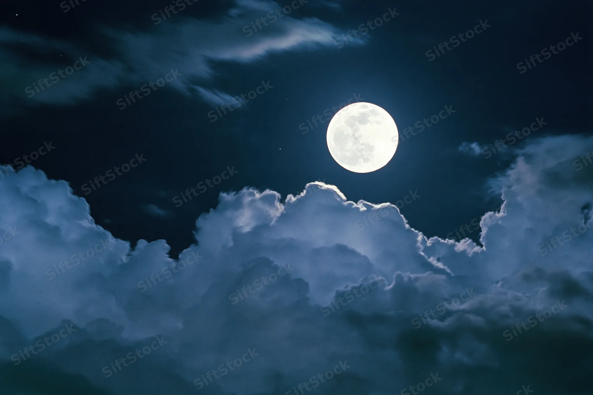 Full moon glowing bright white against deep midnight sky with clouds