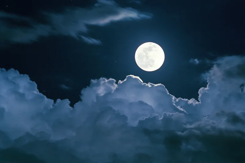 Full moon glowing bright white against deep midnight sky with clouds