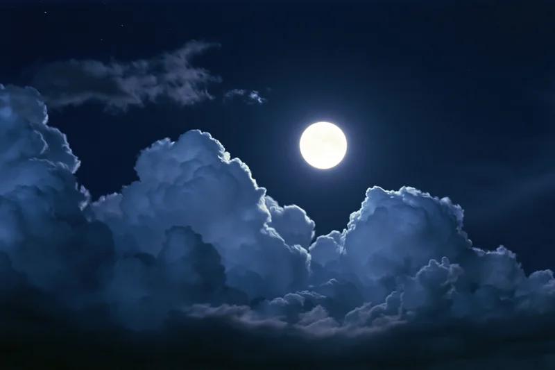 Full moon glowing bright white against deep midnight sky with clouds