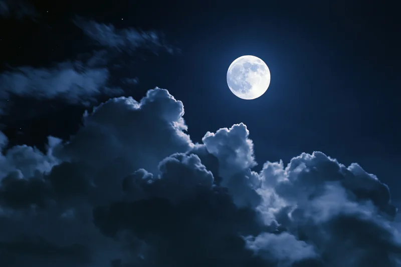 Full moon glowing bright white against deep midnight sky with clouds