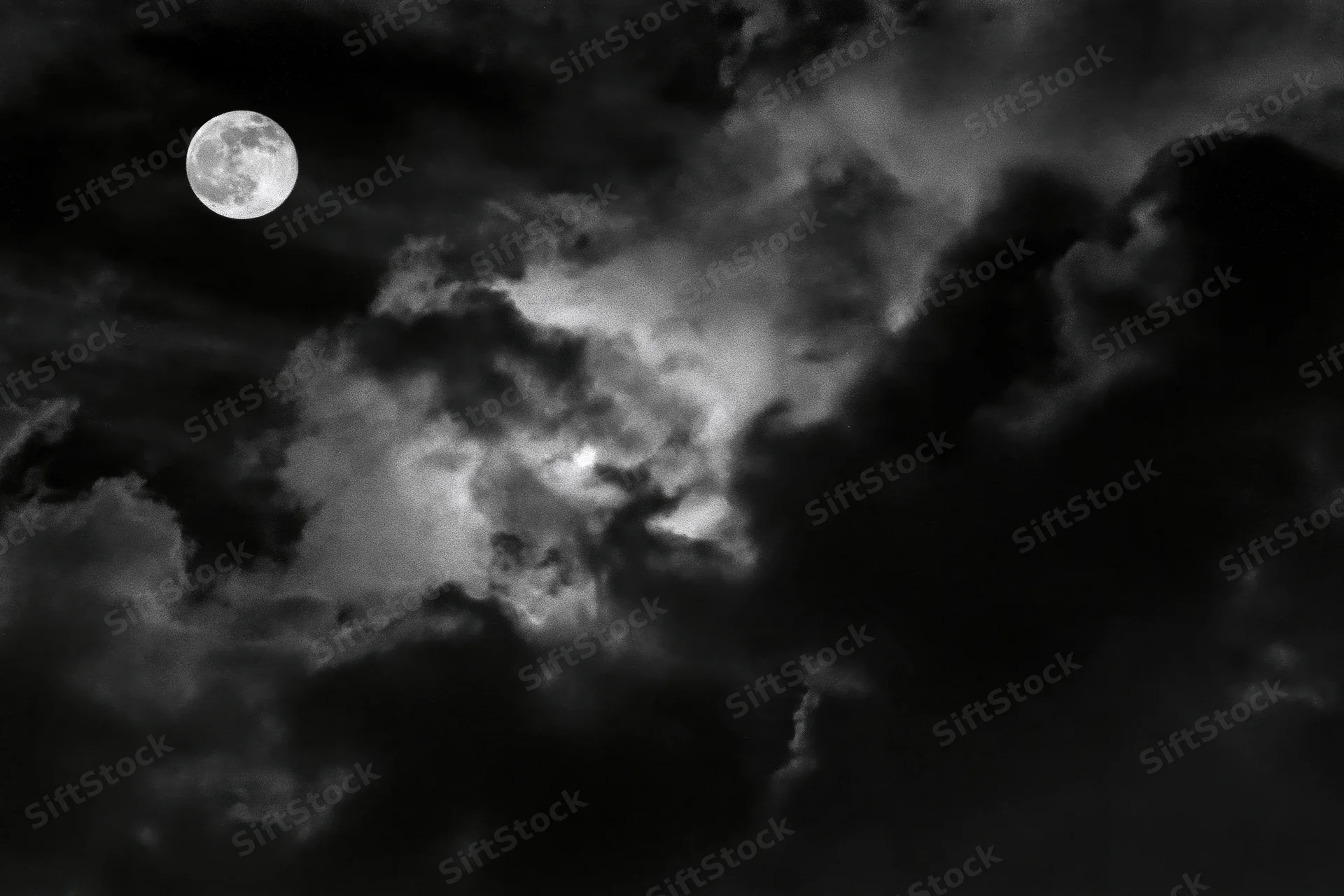 Full moon glowing through dense storm clouds in a dark night sky