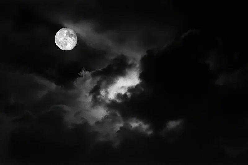 Full moon glowing through dense storm clouds in a dark night sky