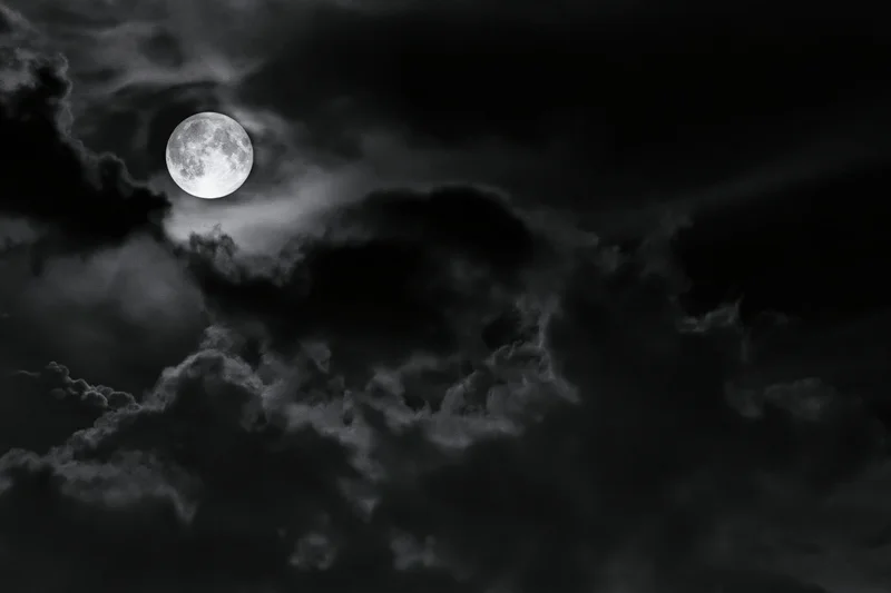 Full moon glowing through dense storm clouds in a dark night sky