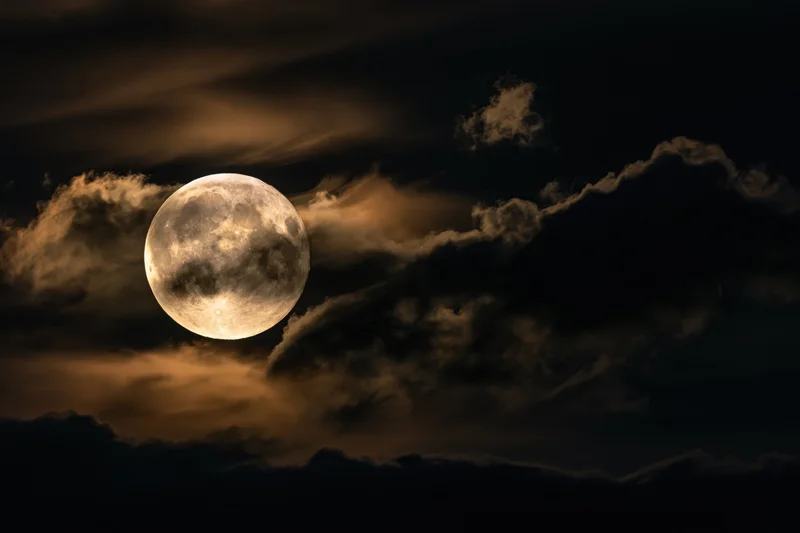 Full moon glowing through drifting clouds in the night sky
