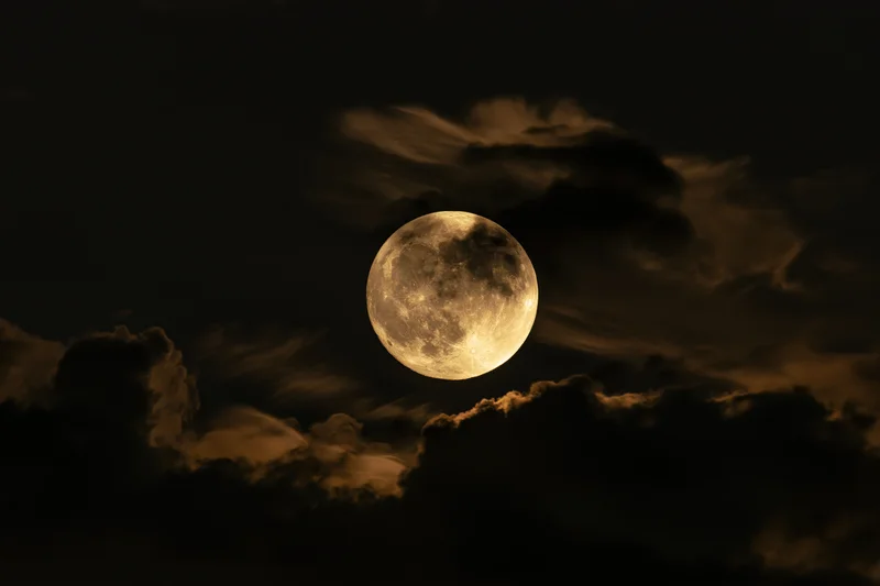 Full moon glowing in dark sky partially veiled by drifting clouds