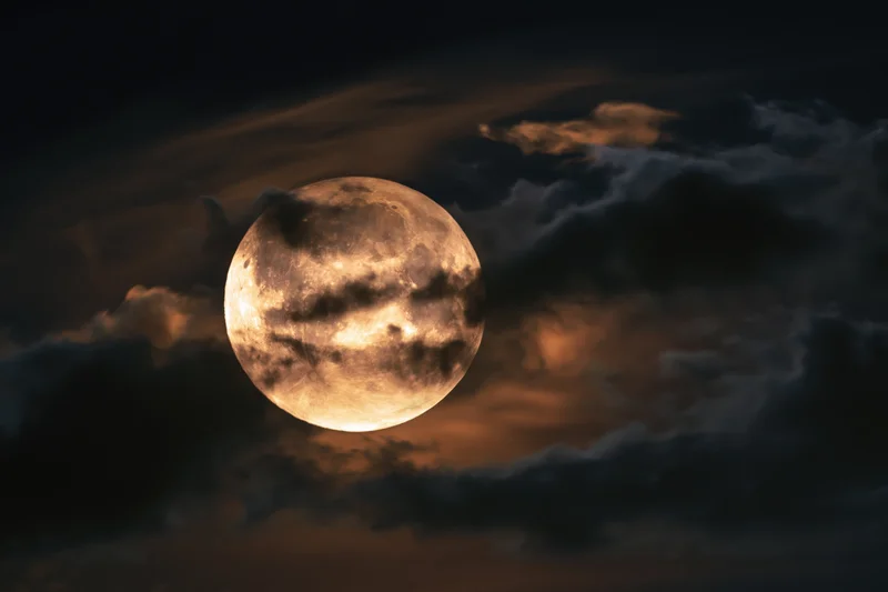 Full moon partially veiled by drifting clouds in the night sky