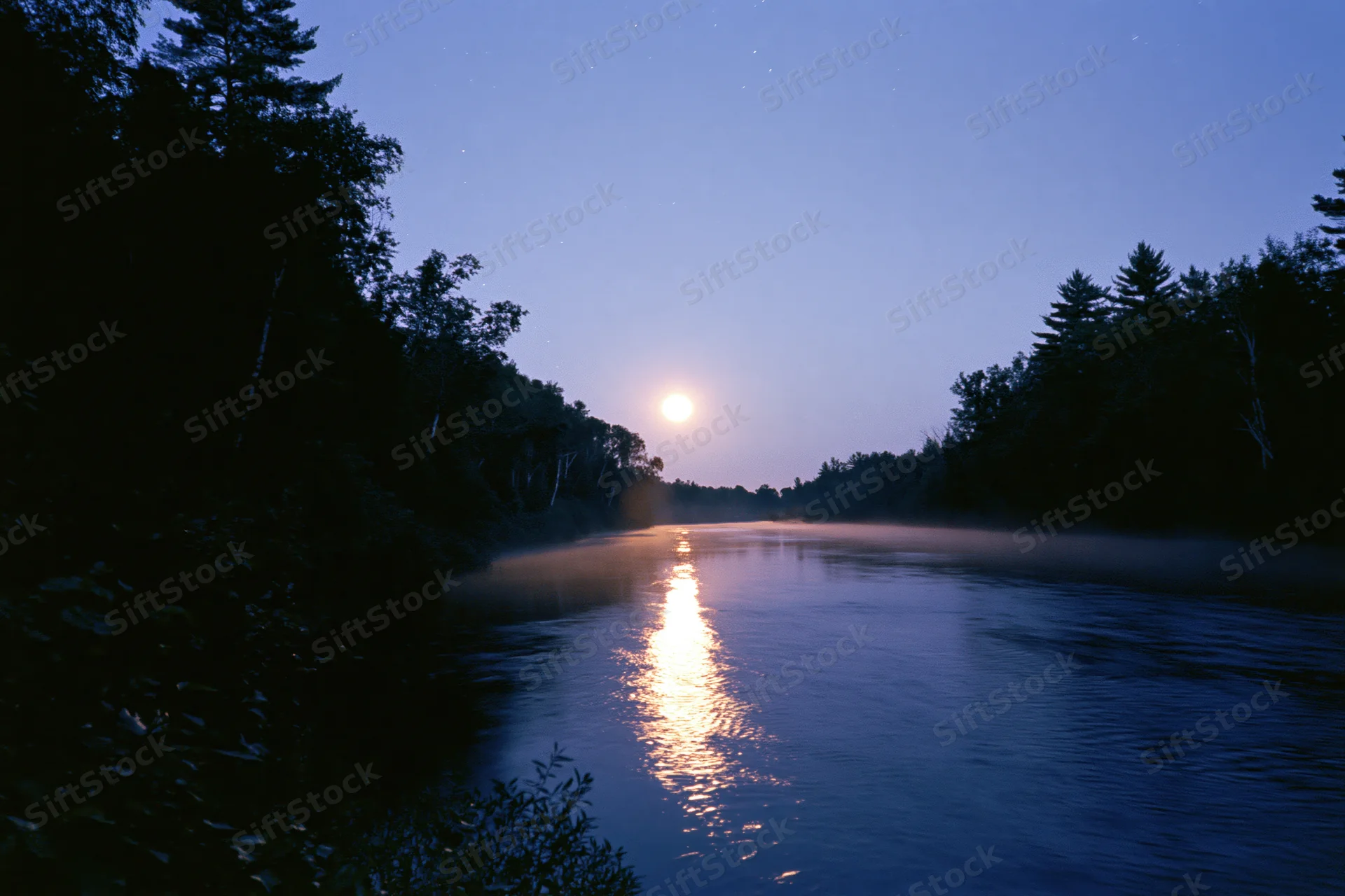 Full moon rising over calm river at night with moonlight reflecting on water surrounded by dark forest