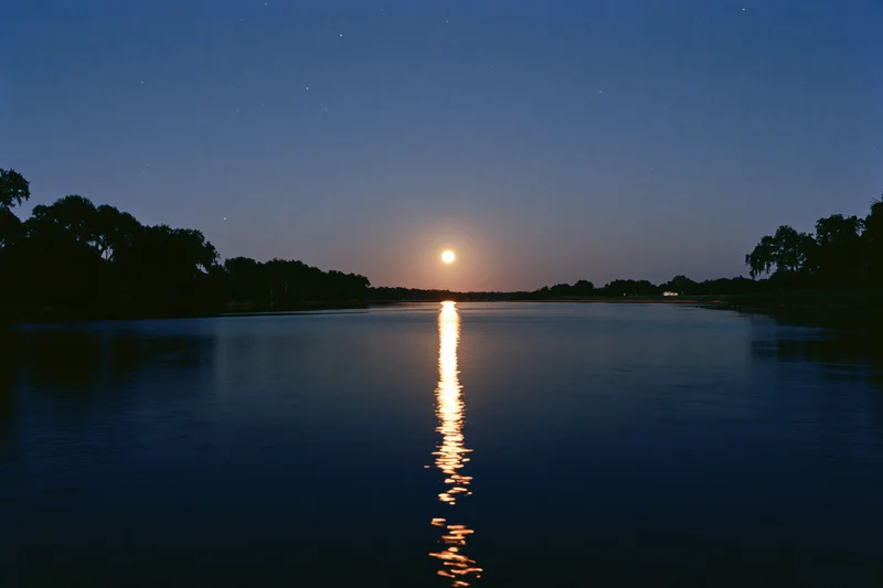 Full moon rising over calm river at night with reflection on water surface
