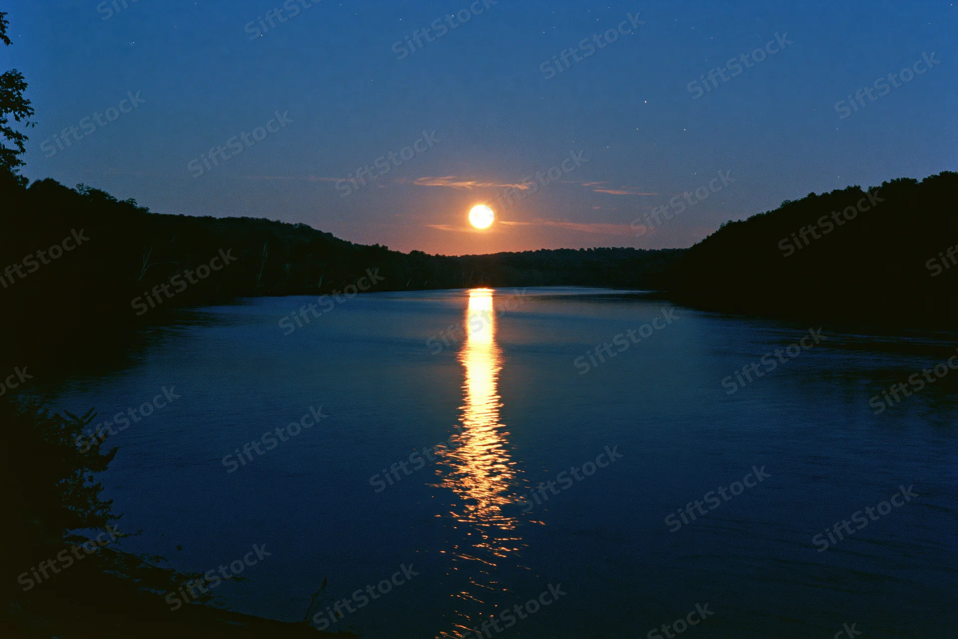 Full moon rising over calm river at night with reflection on water surface