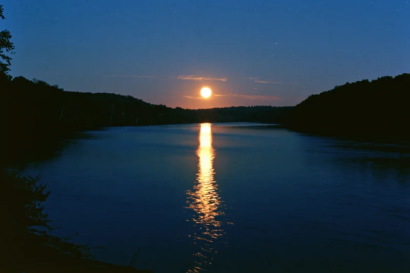 Full moon rising over calm river at night with reflection on water surface