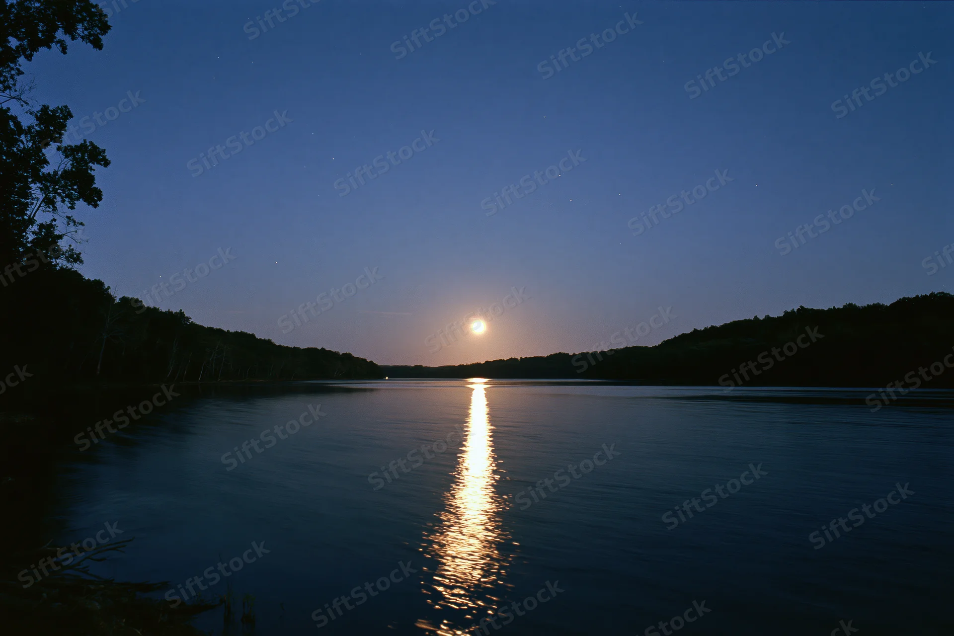 Full moon rising over calm river at night with moonlight reflecting on water surface