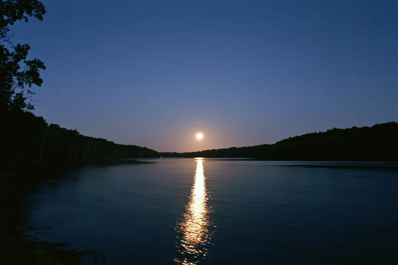 Full moon rising over calm river at night with moonlight reflecting on water surface