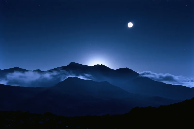 Full moon rising over dark mountain silhouette range at night