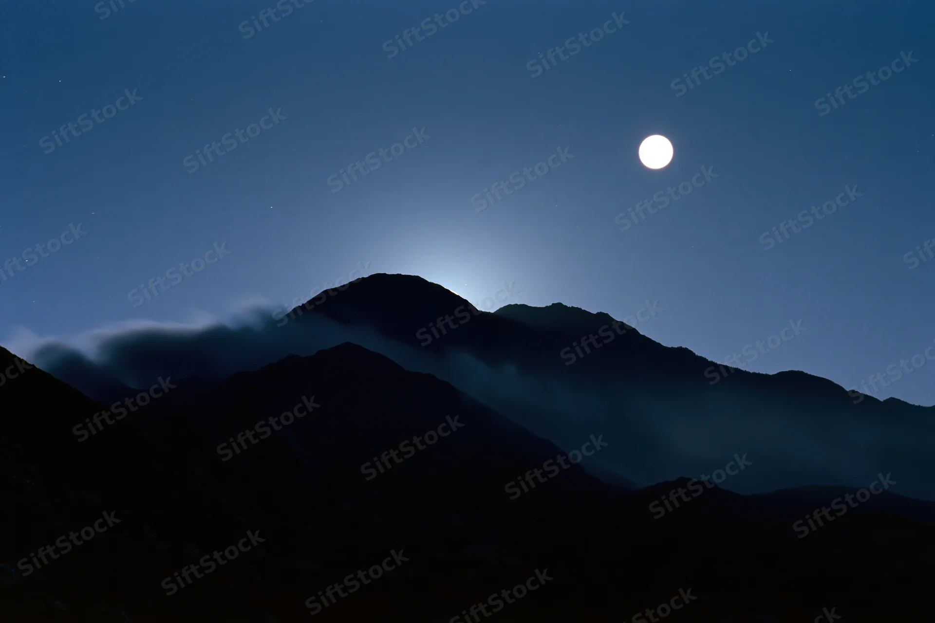 Full moon rising over dark mountain silhouette range at night