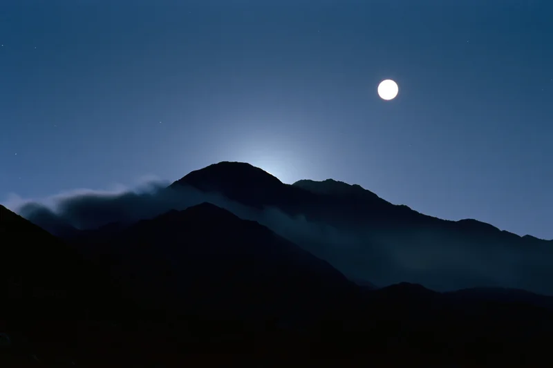 Full moon rising over dark mountain silhouette range at night