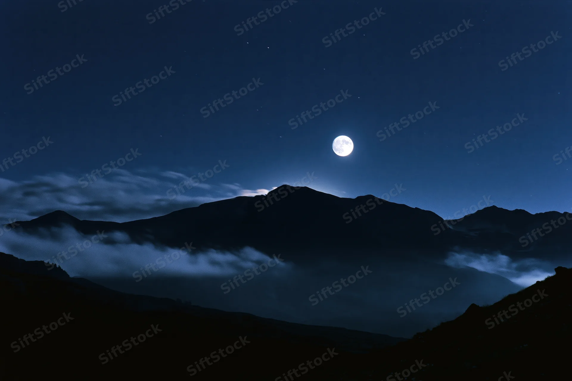 Full moon rising over dark mountain silhouette range at night
