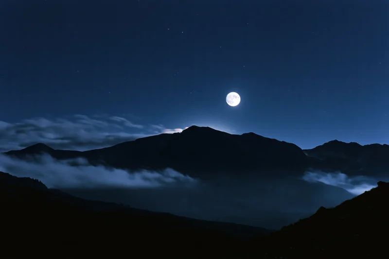 Full moon rising over dark mountain silhouette range at night