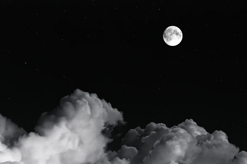 Full moon rising above billowing cumulus clouds in a starry night sky