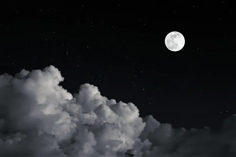 Full moon rising above billowing cumulus clouds in a starry night sky