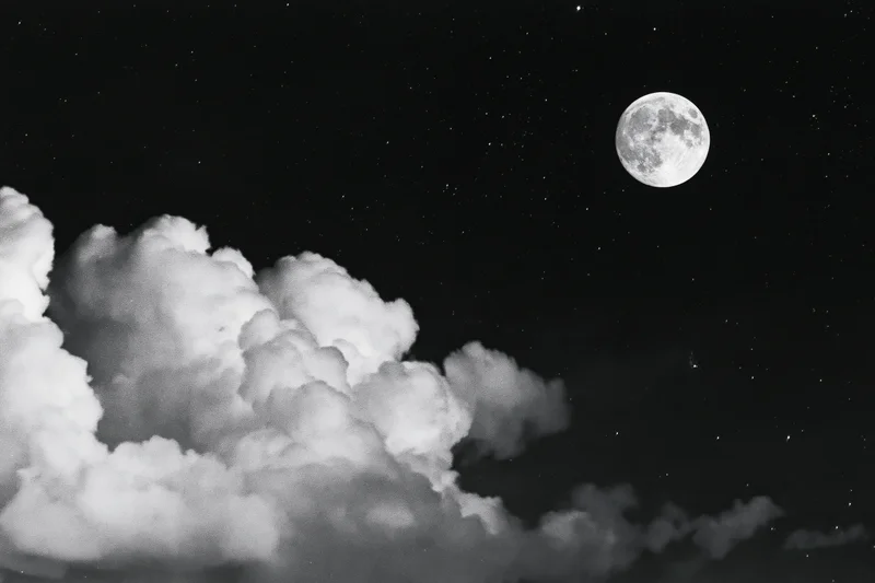 Full moon rising above billowing cumulus clouds in a starry night sky
