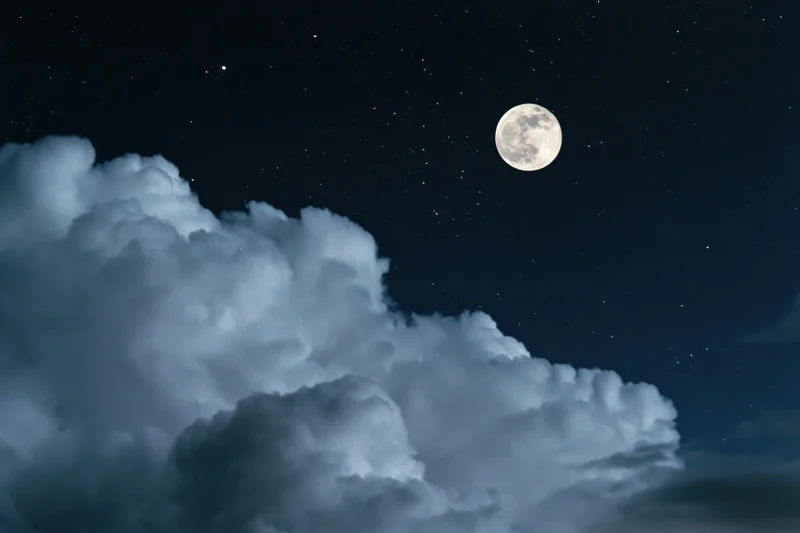 Full moon rising over billowing cumulus clouds against a deep night sky