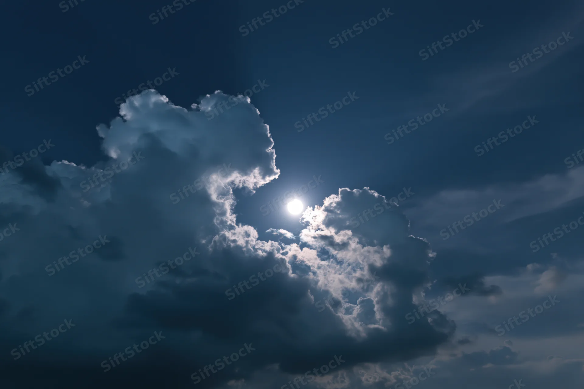Full moon rising through broken cumulus clouds at night