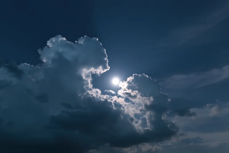 Full moon rising through broken cumulus clouds at night