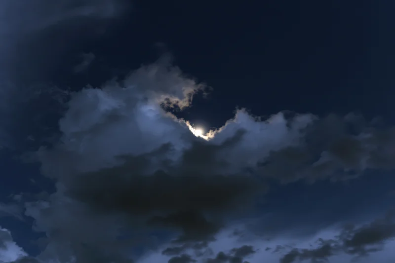Full moon glowing through broken cumulus clouds at night