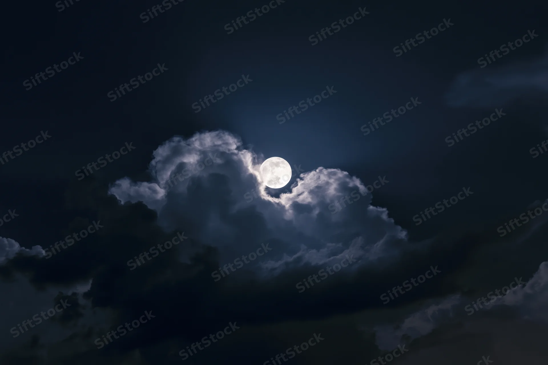 Full moon rising through broken cumulus clouds at night
