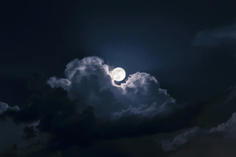 Full moon rising through broken cumulus clouds at night