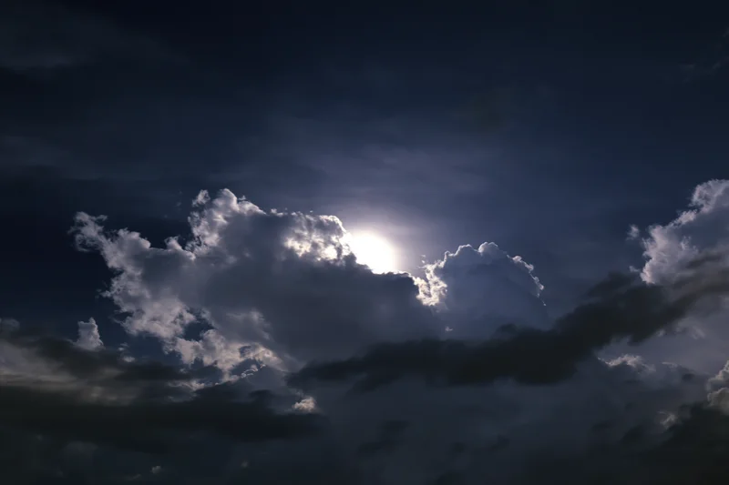Full moon rising through broken cumulus clouds at night