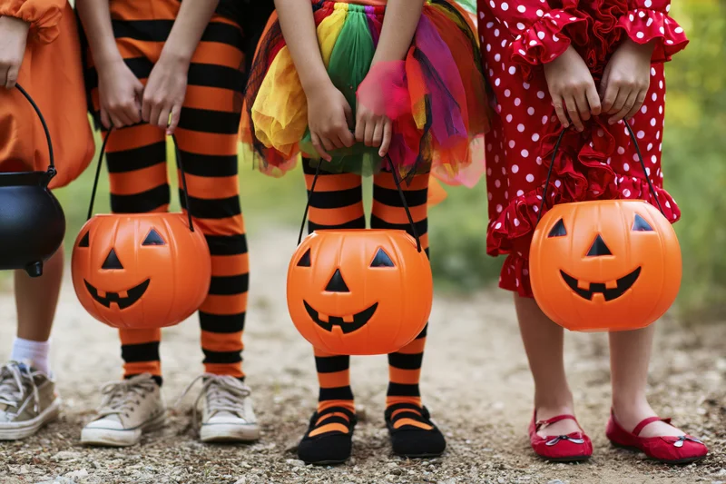 Children in halloween costumes holding plastic jack-o-lantern buckets outdoors