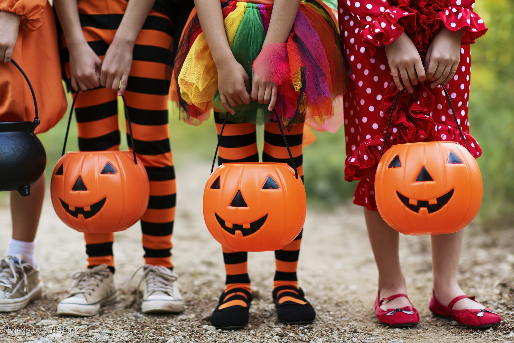 Children in halloween costumes holding plastic jack-o-lantern buckets outdoors