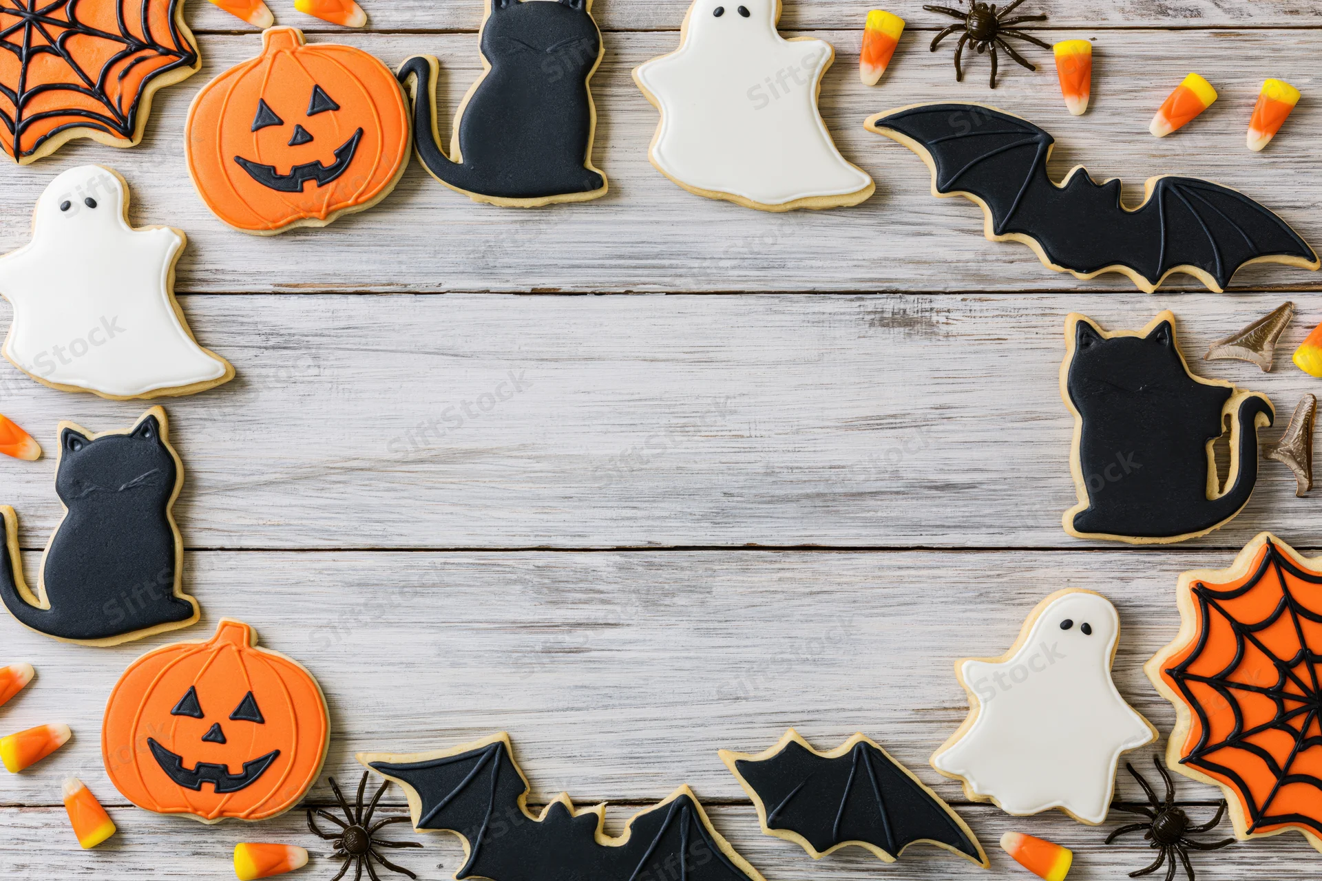 Halloween-themed sugar cookies arranged in a border on a wooden surface with copyspace in the center