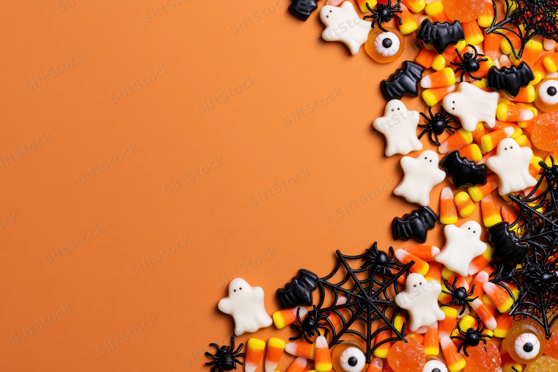 Halloween candy and decorations arranged along the right side on orange background