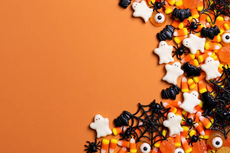 Halloween candy and decorations arranged along the right side on orange background