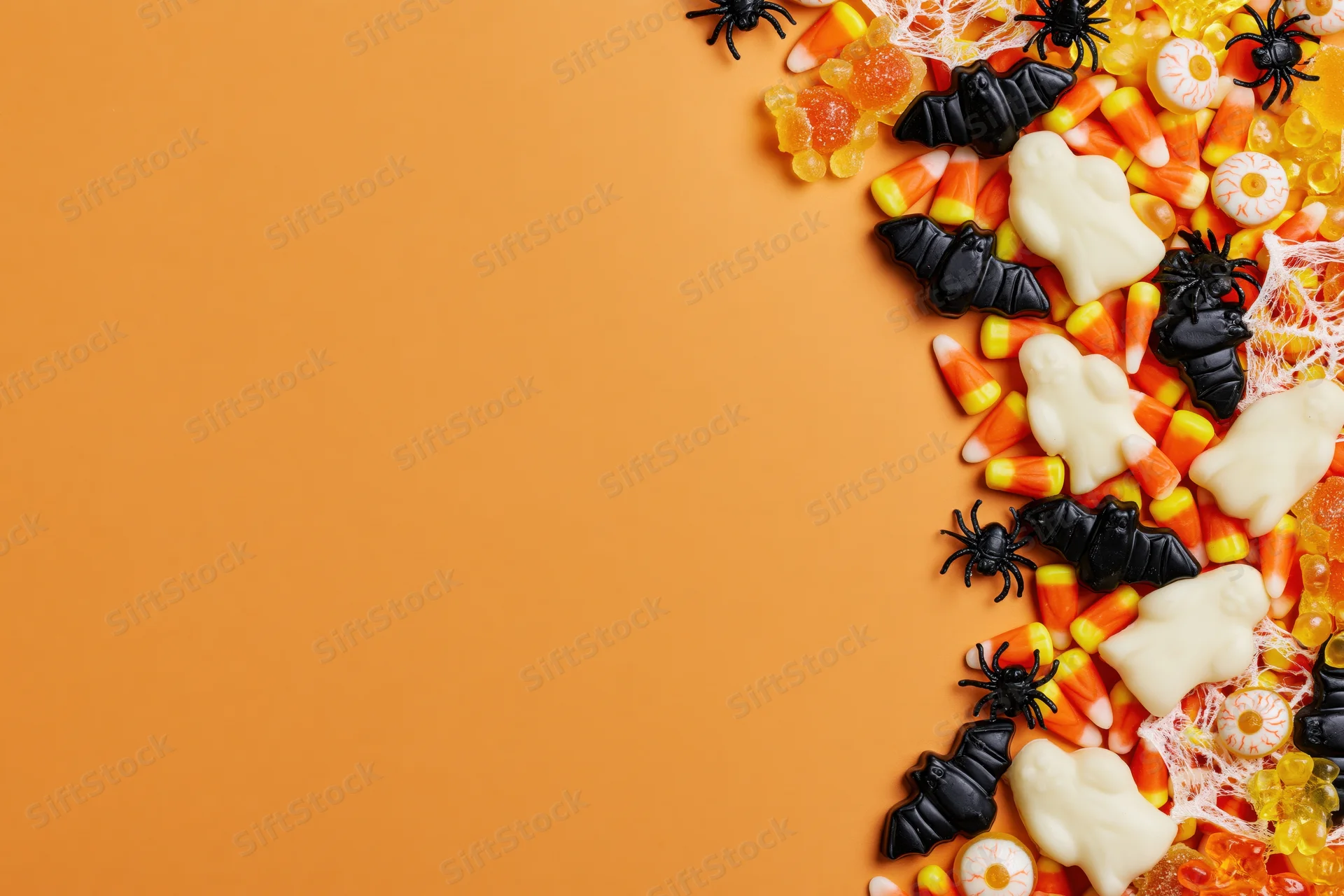Halloween candy and decorations arranged along the right side on orange background with copyspace