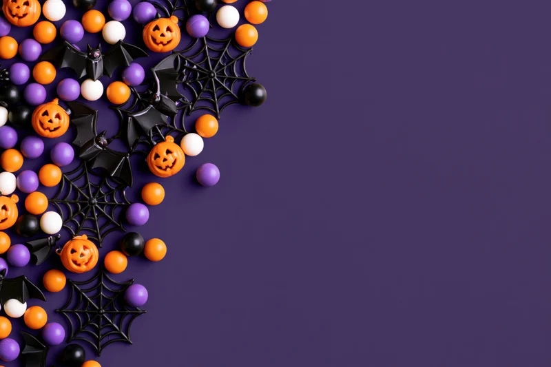 Halloween decorations and candy arranged on left side of purple background with copyspace
