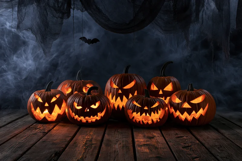 Carved jack-o-lanterns glowing on a wooden floor with smoke and cobwebs in the background