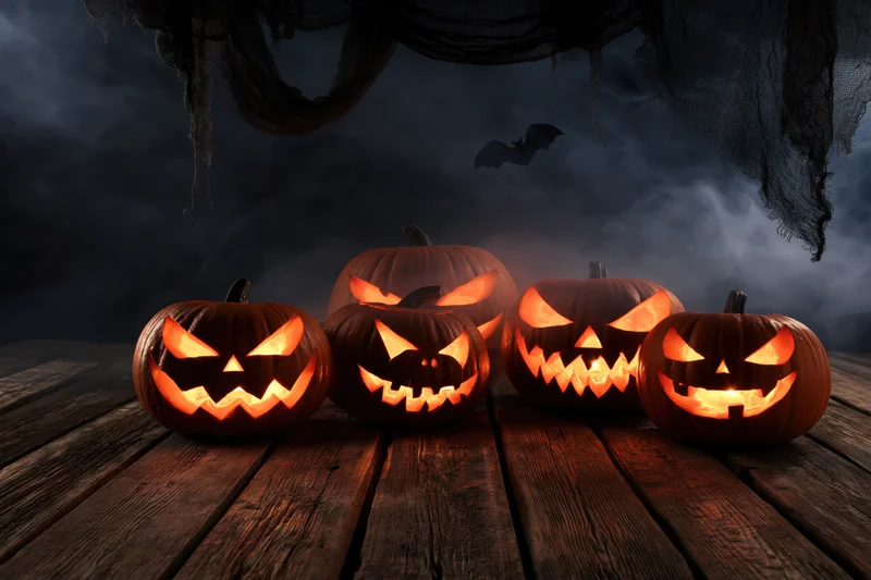 Carved jack-o-lanterns glowing on a wooden table under dark cobwebs with a bat flying in the background