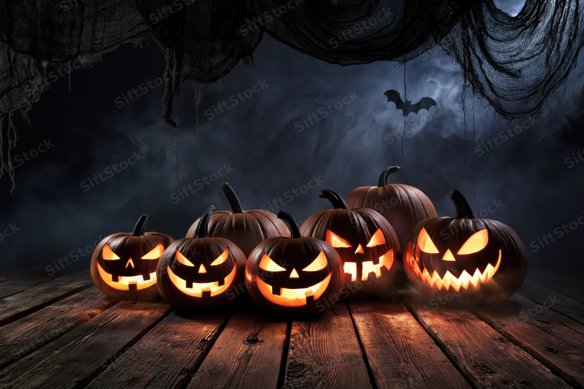 Carved pumpkins with glowing faces arranged on a wooden floor under hanging cobwebs at night