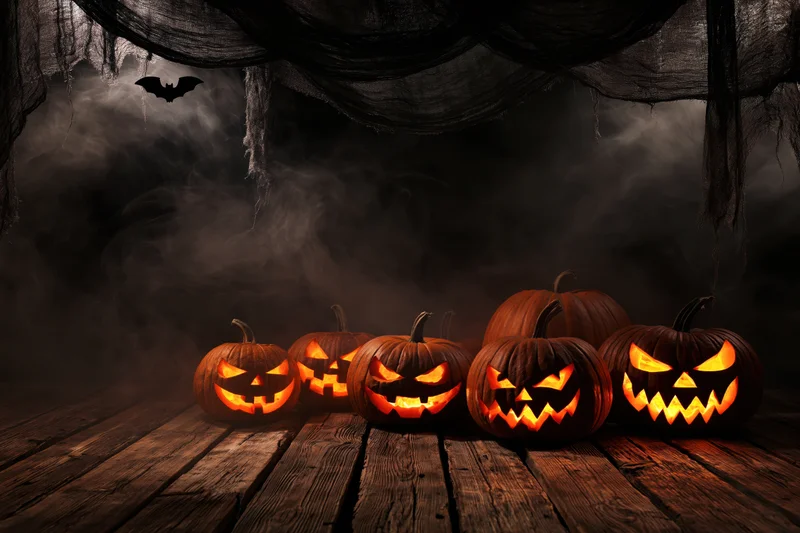 Carved pumpkins with glowing faces arranged on a wooden floor under hanging cobwebs and smoke