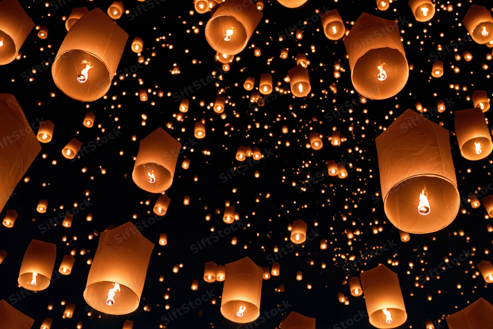 Sky lanterns floating upward in the night sky during a festival