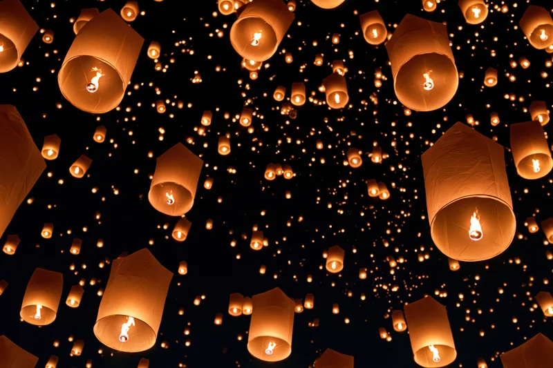 Sky lanterns floating upward in the night sky during a festival